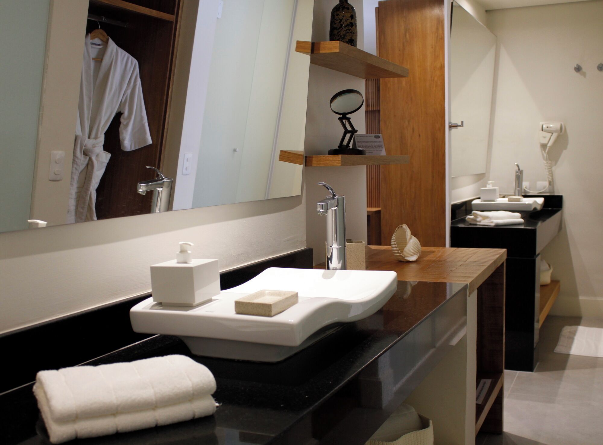Une salle de bain moderne avec un grand miroir, un plan de toilette noir, un lavabo blanc et un meuble-lavabo en bois.