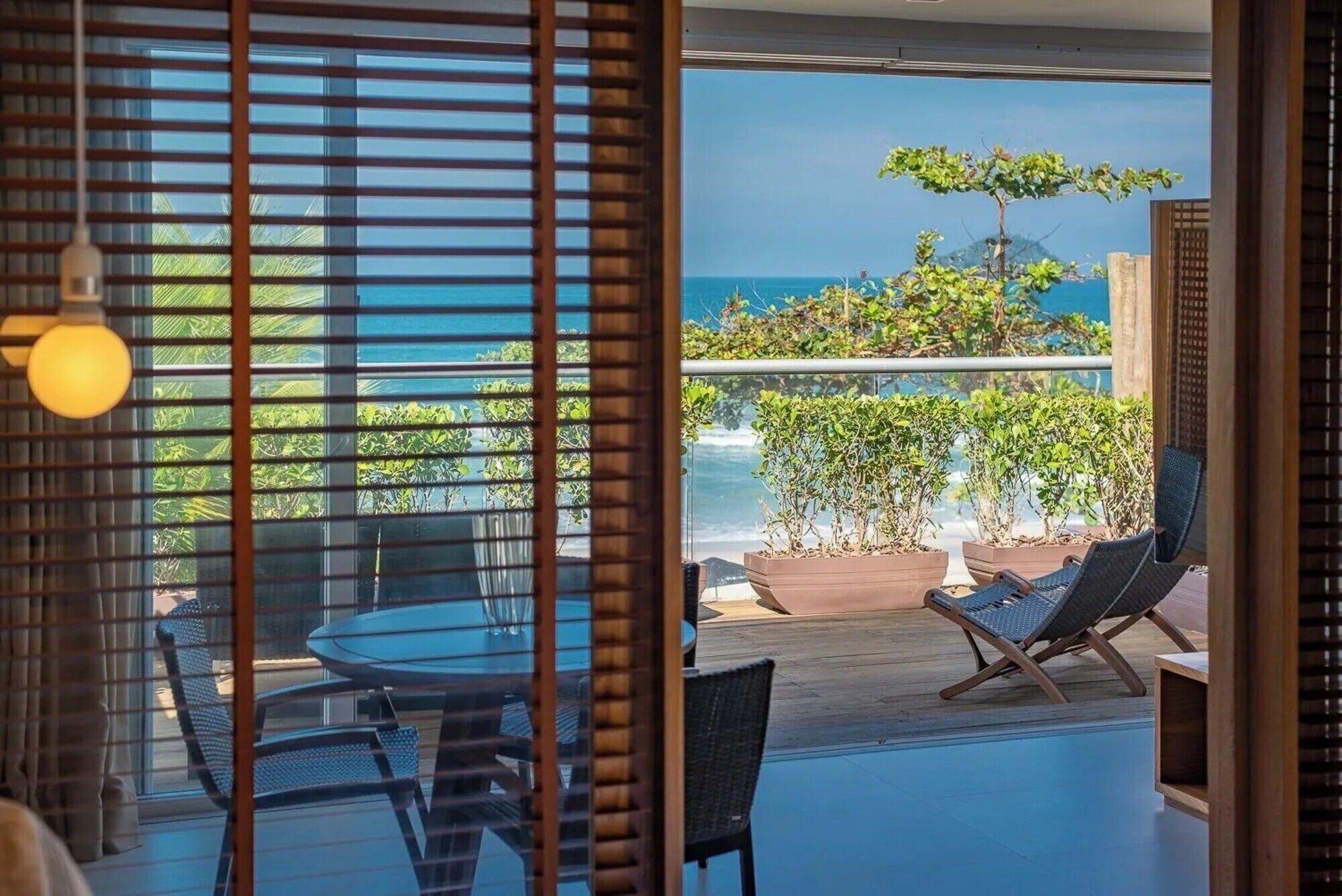 Un balcon avec vue sur l’océan, une table avec des chaises et une plante en pot.