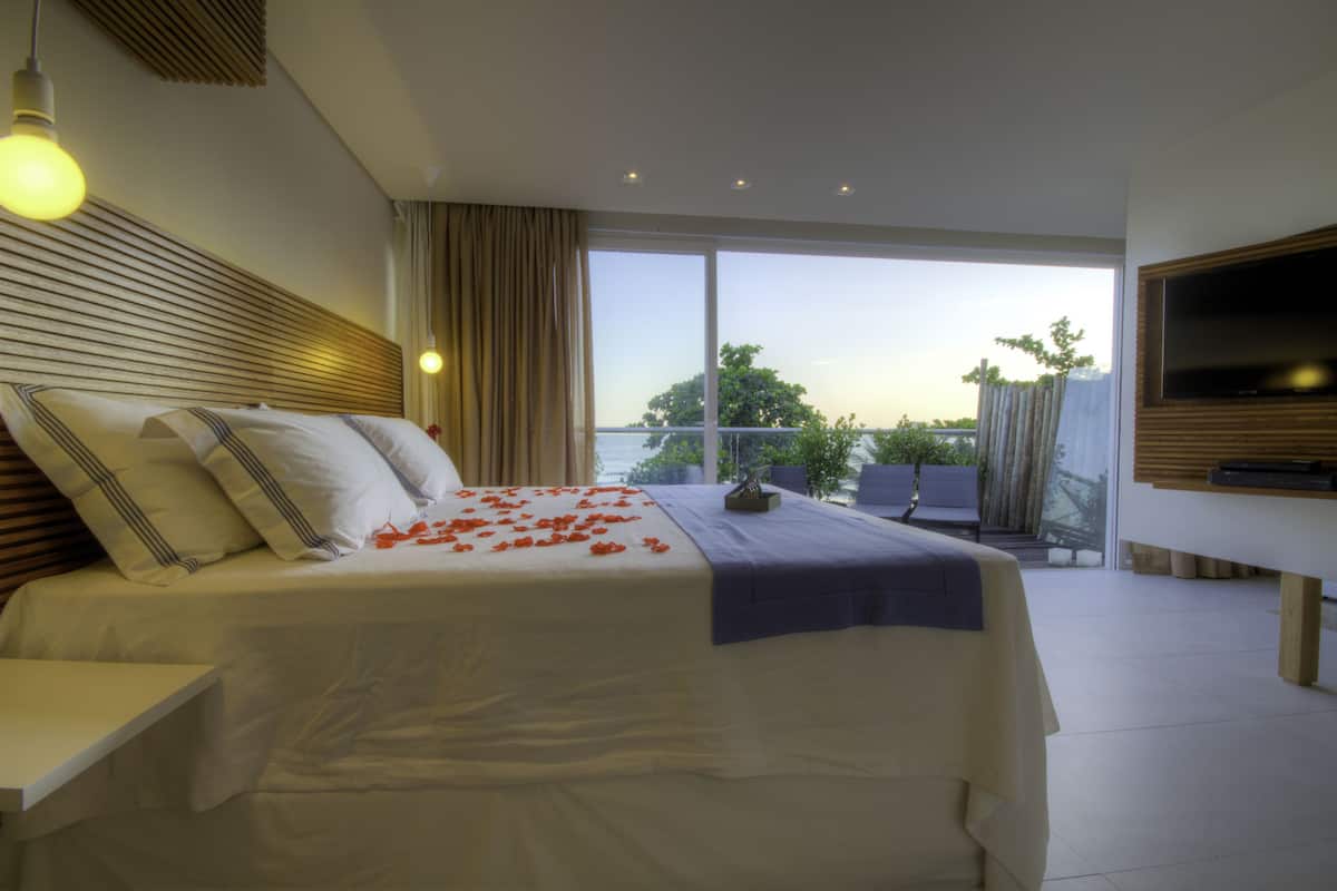 A modern hotel room with a large bed, a TV, and a balcony with a view.