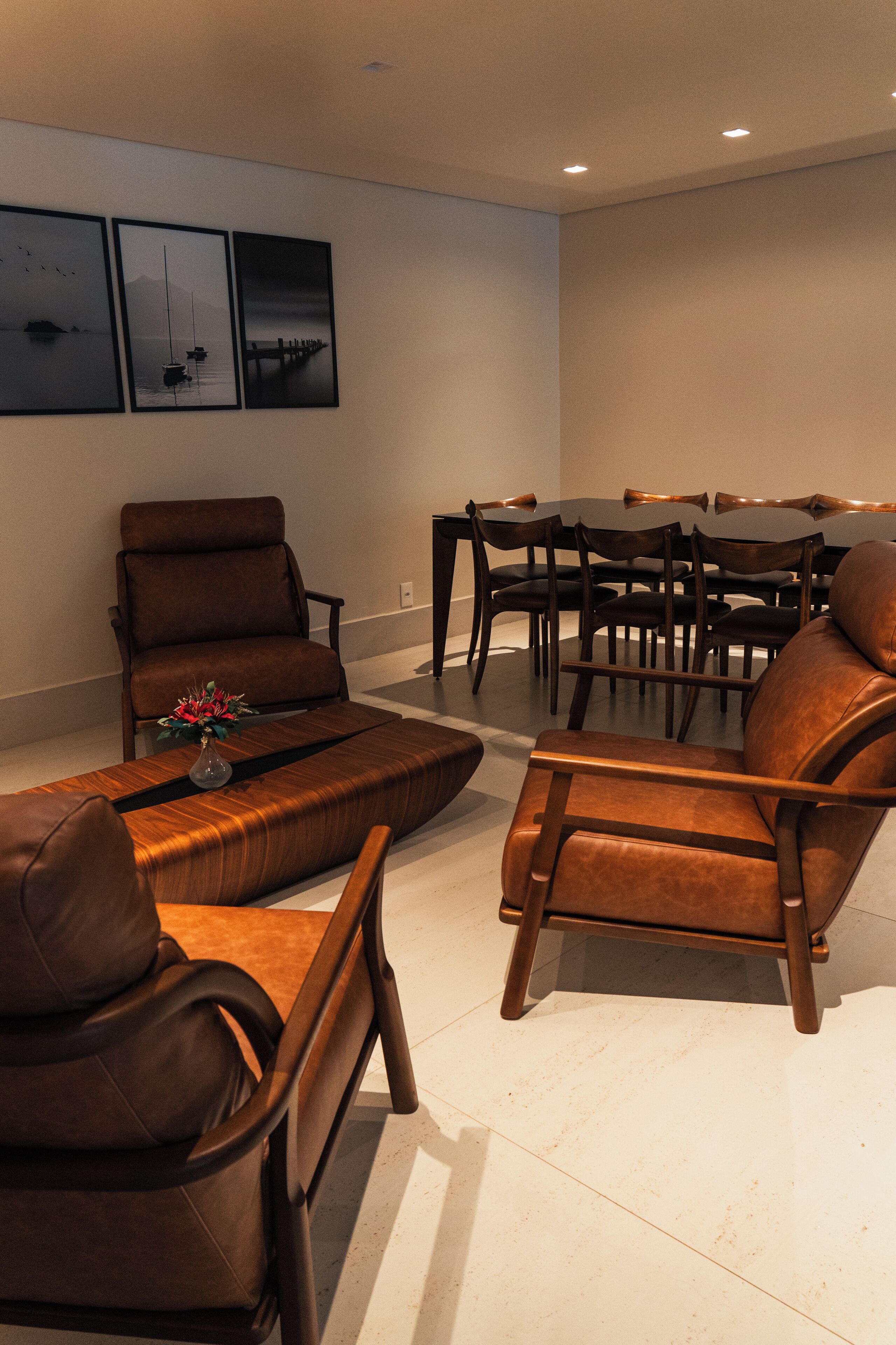 Een moderne woonkamer met een bruine leren bank, een houten salontafel met een vaas, en een eethoek met een houten tafel en stoelen.