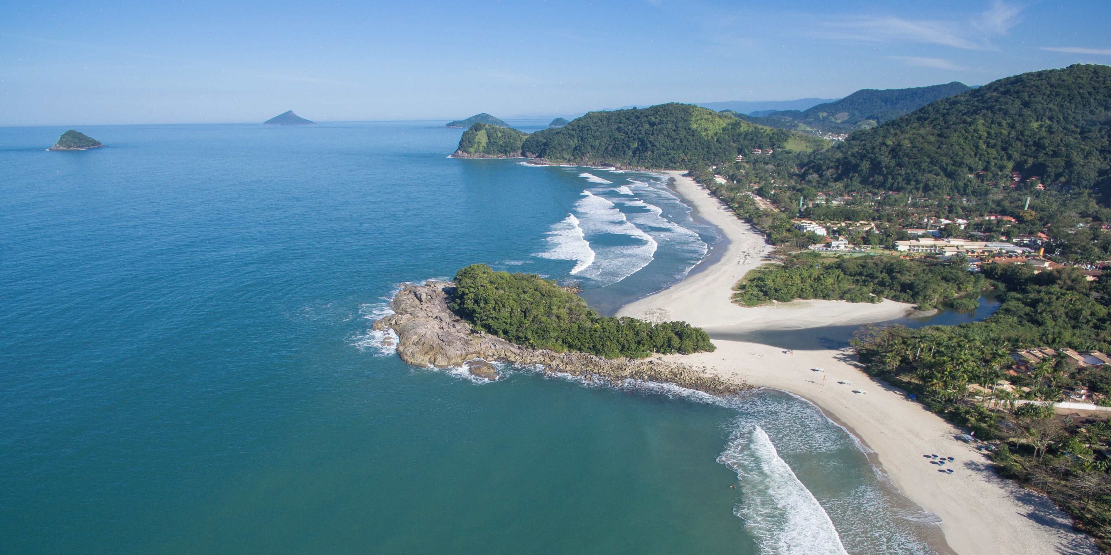 An aerial view of a coastal area with a beach, rocky outcrops, and surrounding hills.