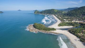 An aerial view of a coastal area with a beach, rocky outcrops, and surrounding hills.