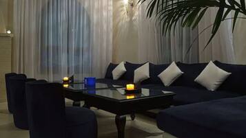 A modern living room with a dark blue sofa set, a glass coffee table, and a large potted plant.