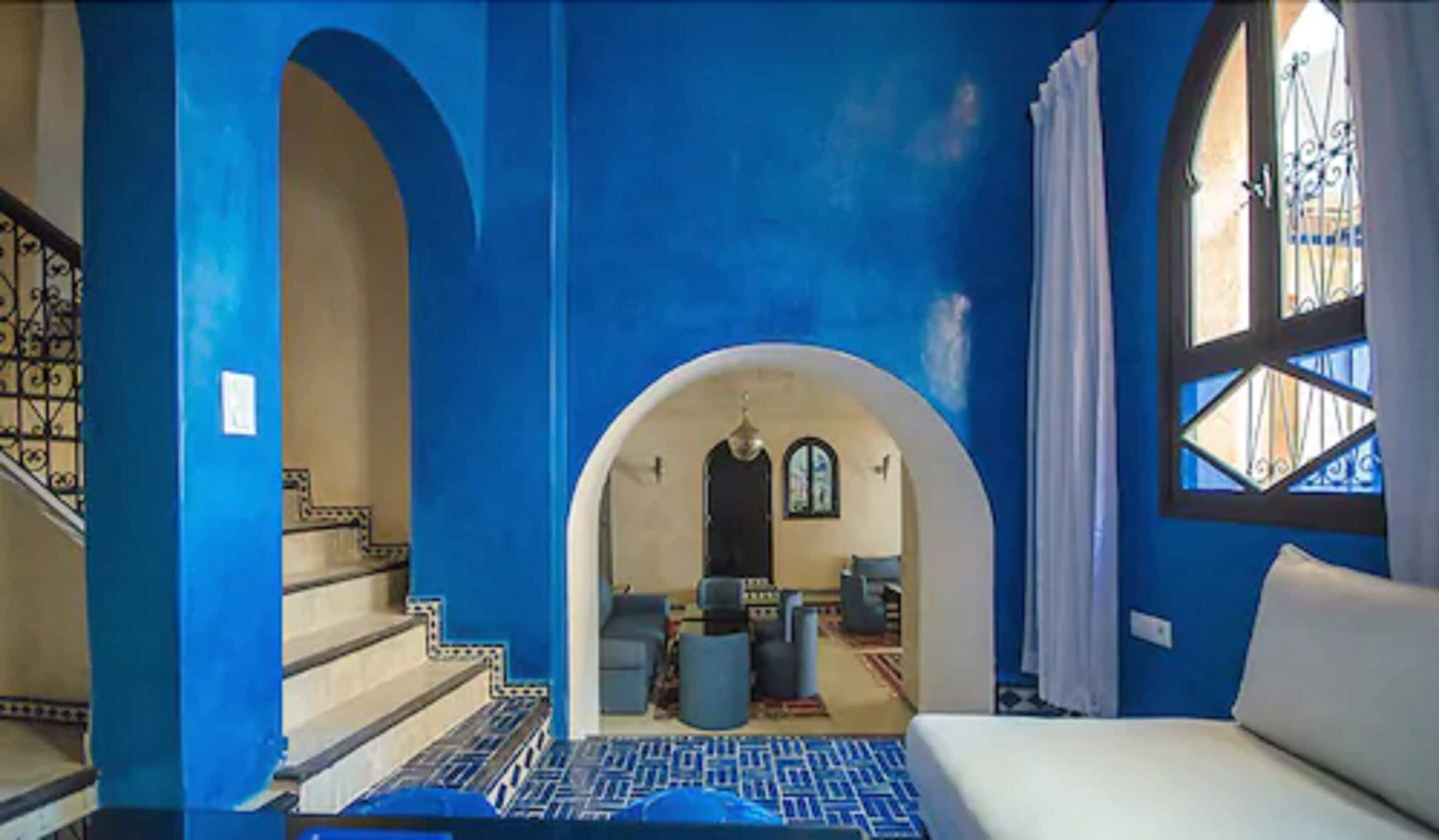 Una habitación con decoración azul, que incluye una cama, una escalera y vistas a otra habitación a través de un arco.