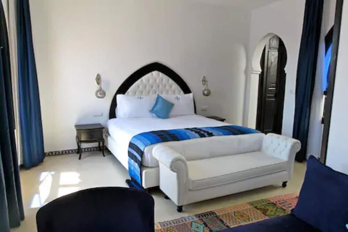 Una habitación de hotel con cama, mesita de noche, sofá y alfombra estampada.