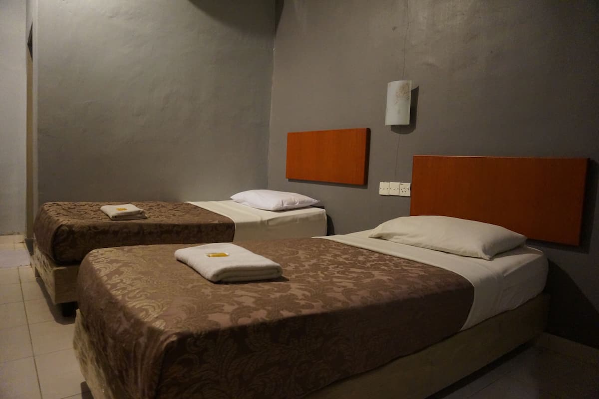 A hotel room with two single beds, each with a brown patterned bedspread and white pillows.