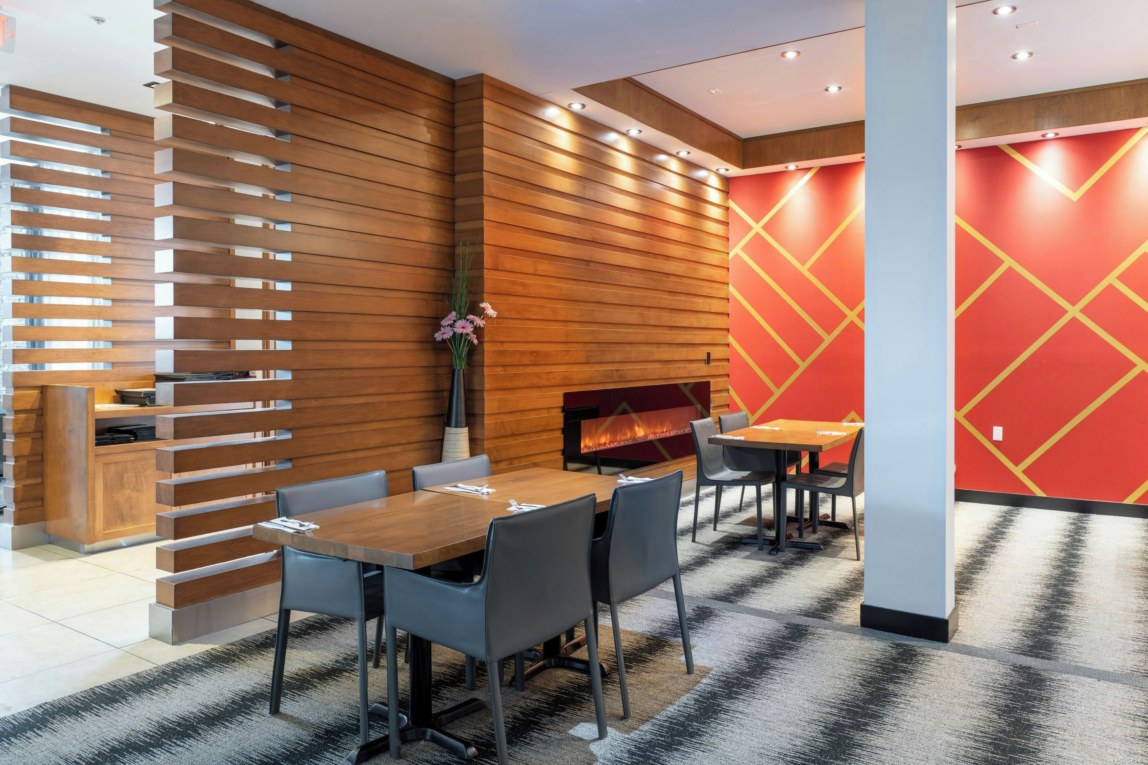 A modern interior with a wooden slatted wall, a fireplace, and a red geometric wall design.