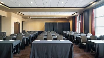 Ein Konferenzraum mit Tischen und Stühlen, einer Uhr an der Wand und einem großen Fenster mit Vorhängen.