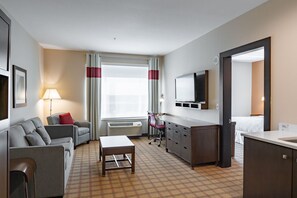 A hotel room with a sofa, a small table, a desk, a chair, a bed, a TV, a mirror, and a window with curtains. - Four Points by Sheraton Edmonton International Airport (Nisku)