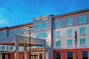 Et hotel i flere etager med en moderne facade, store vinduer og tydelig skiltning med 'FOUR POINTS BY SHERATON'.