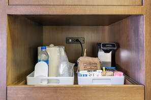 A storage compartment with a coffee maker, a bottle of milk, a coffee bag, and a box of coffee pods. - Four Points by Sheraton Edmonton International Airport (Nisku)