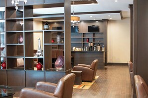 A modern interior with leather chairs, a bar area, and shelves with decorative items. - Four Points by Sheraton Edmonton International Airport (Nisku)