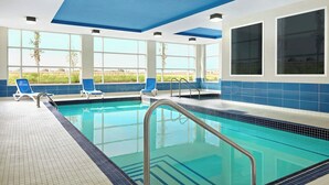 A swimming pool with clear blue water, surrounded by blue and white tiled walls, and large windows offering a view of the outdoors. - Four Points by Sheraton Edmonton International Airport (Nisku)