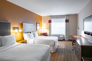 Habitación de hotel con dos camas, un escritorio, una silla, un televisor y una ventana con cortinas.