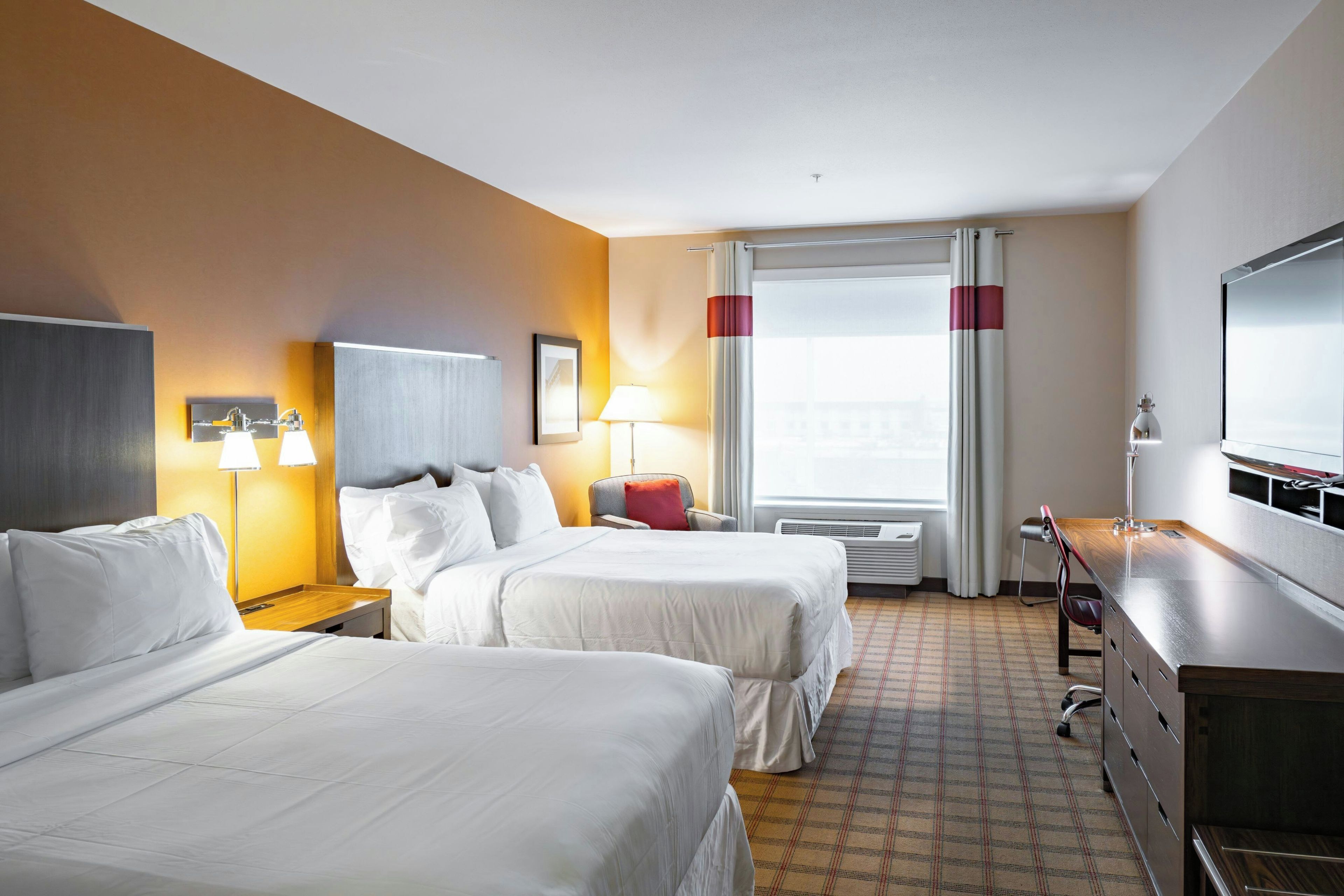A hotel room with two beds, a desk, a chair, a TV, and a window with curtains.