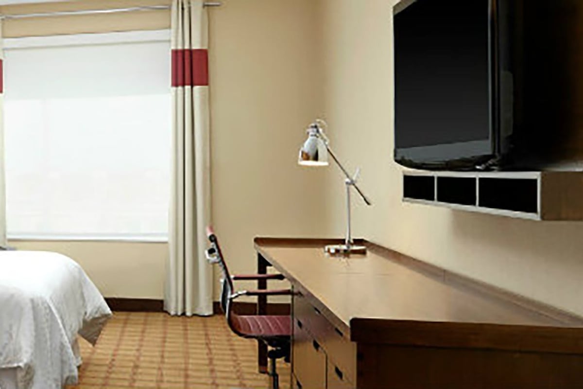 A hotel room with two beds, a desk, a chair, a TV, and a window with curtains.