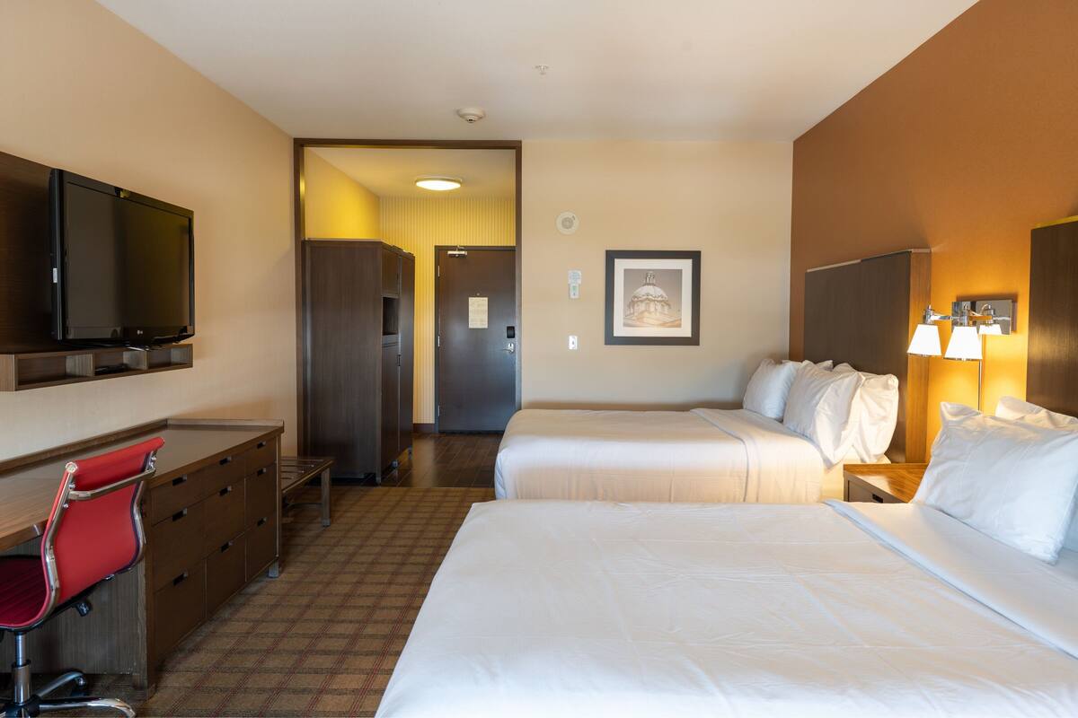 A hotel room with two beds, a desk with a chair, a television, and a framed picture on the wall.