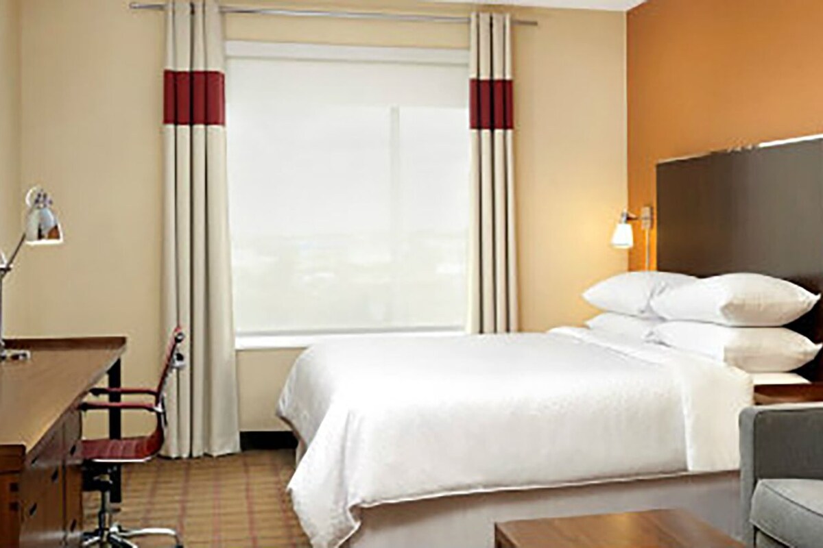 A hotel room with a bed, a desk, a television, a sofa, and a framed picture on the wall.