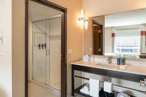 A modern bathroom with a glass shower enclosure, a dark wooden vanity, and a large mirror. - Four Points by Sheraton Edmonton International Airport (Nisku)