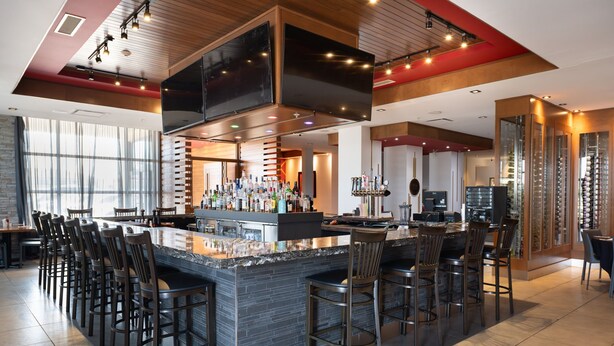 A modern bar area with a central island, bar stools, and a variety of bottles. - Four Points by Sheraton Edmonton International Airport (Nisku)