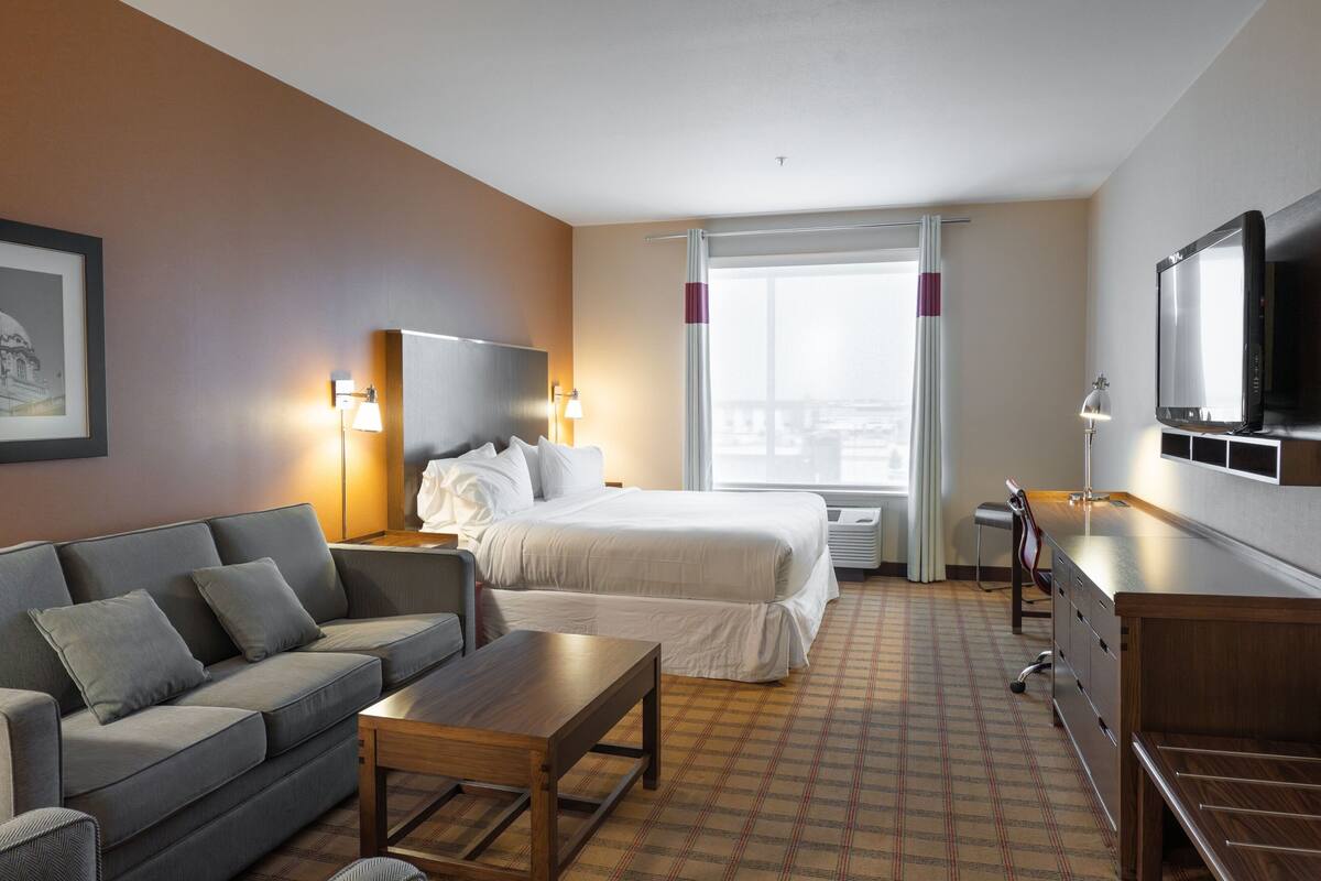 A hotel room with a bed, a sofa, a desk, a TV, and a window with curtains.