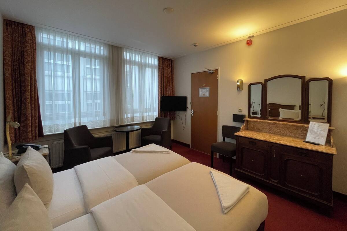 Ein Hotelzimmer mit zwei Betten, einem Schreibtisch, einem Stuhl, einem Fernseher und einem Spiegel.