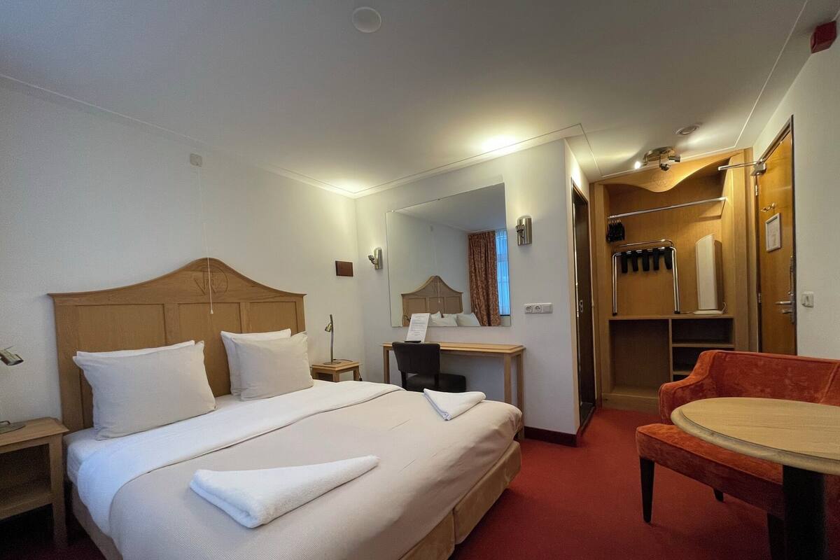 Ein Hotelzimmer mit einem großen Bett, einem Schreibtisch, einem Sessel und einem kleinen Tisch.