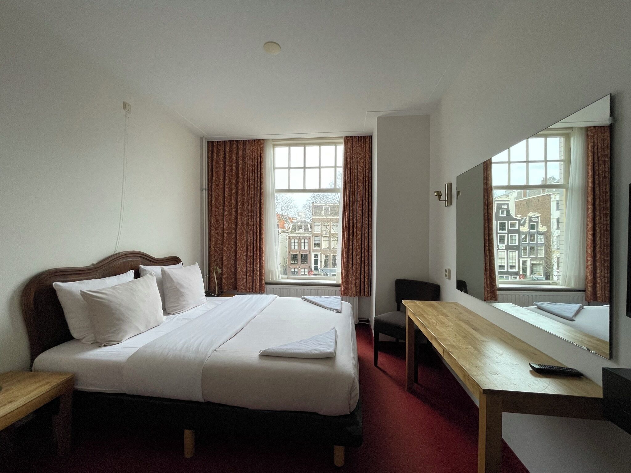 Ein Hotelzimmer mit Bett, Schreibtisch, Stuhl, Spiegel und einem Fenster mit Vorhängen.