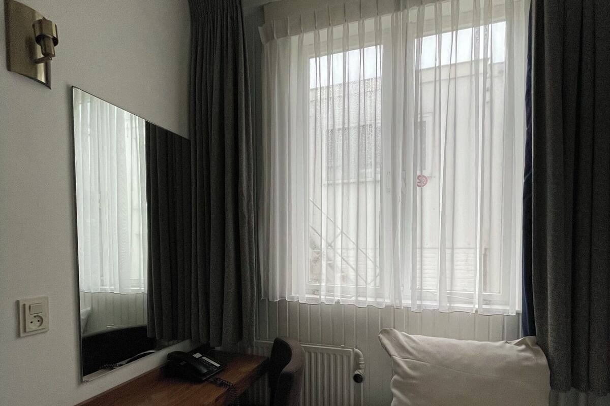 Ein Hotelzimmer mit Bett, Schreibtisch, Telefon, Spiegel und einem Fenster mit Vorhängen.