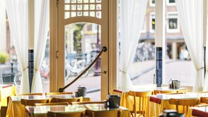 Un caffè con tavoli e sedie gialli, una porta in legno con una finestra e tende bianche.
