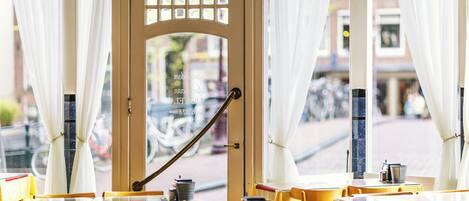 A cafe with yellow tables and chairs, a wooden door with a window, and white curtains.