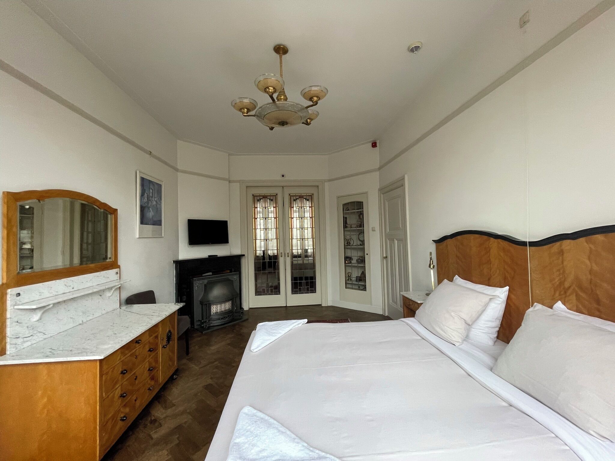 A bedroom with a large bed, a dresser, a television, and a fireplace.