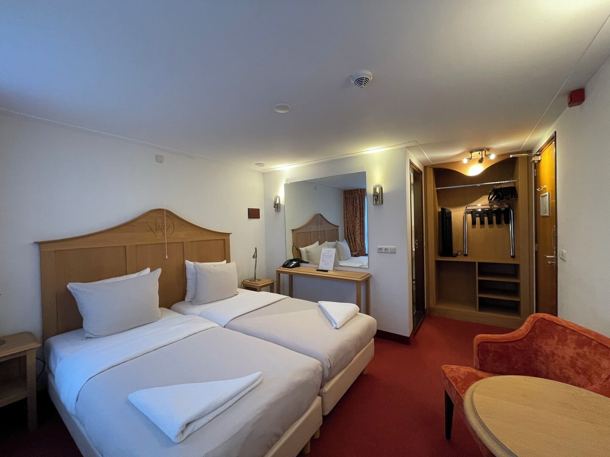 A hotel room with two beds, a desk, a chair, a mirror, and a closet.