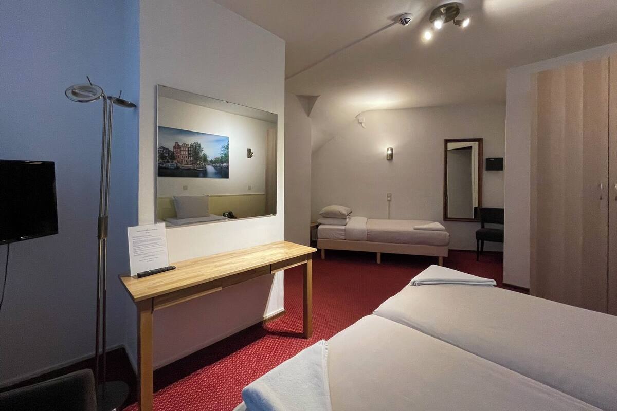 Ein Hotelzimmer mit Bett, Schreibtisch, Spiegel, Fernseher und einem roten Teppich.
