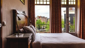 Camera d'albergo con un grande letto, un comodino in legno e vista sulla città attraverso una finestra con tende.