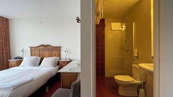 Habitación de hotel con una cama de madera, una mesita auxiliar de mármol, ducha y retrete.