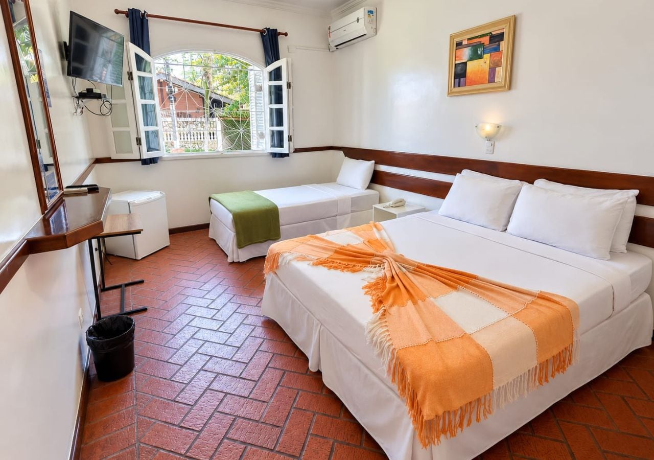 Una habitación de hotel con cama, una mesita, un televisor y un ventanal con cortinas.