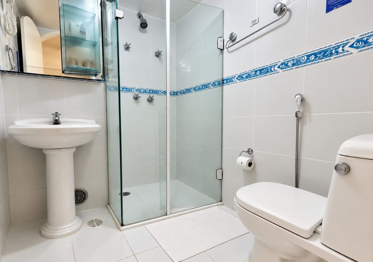 Un baño con cabina de ducha de vidrio, lavamanos sobre pedestal y un inodoro.