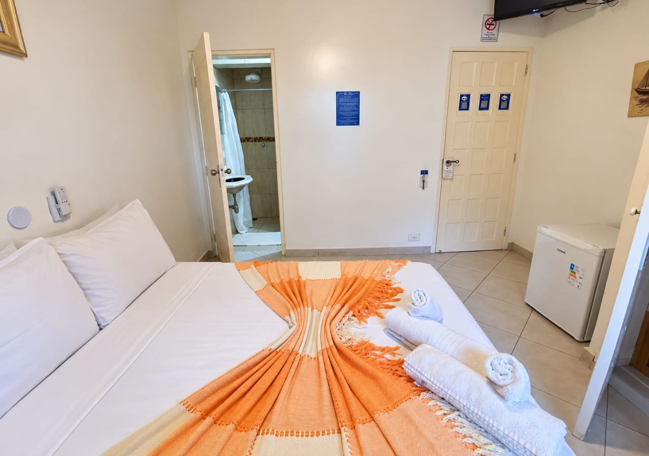 A hotel room with a bed, a small refrigerator, a bathroom with a shower, and a door with a sign.