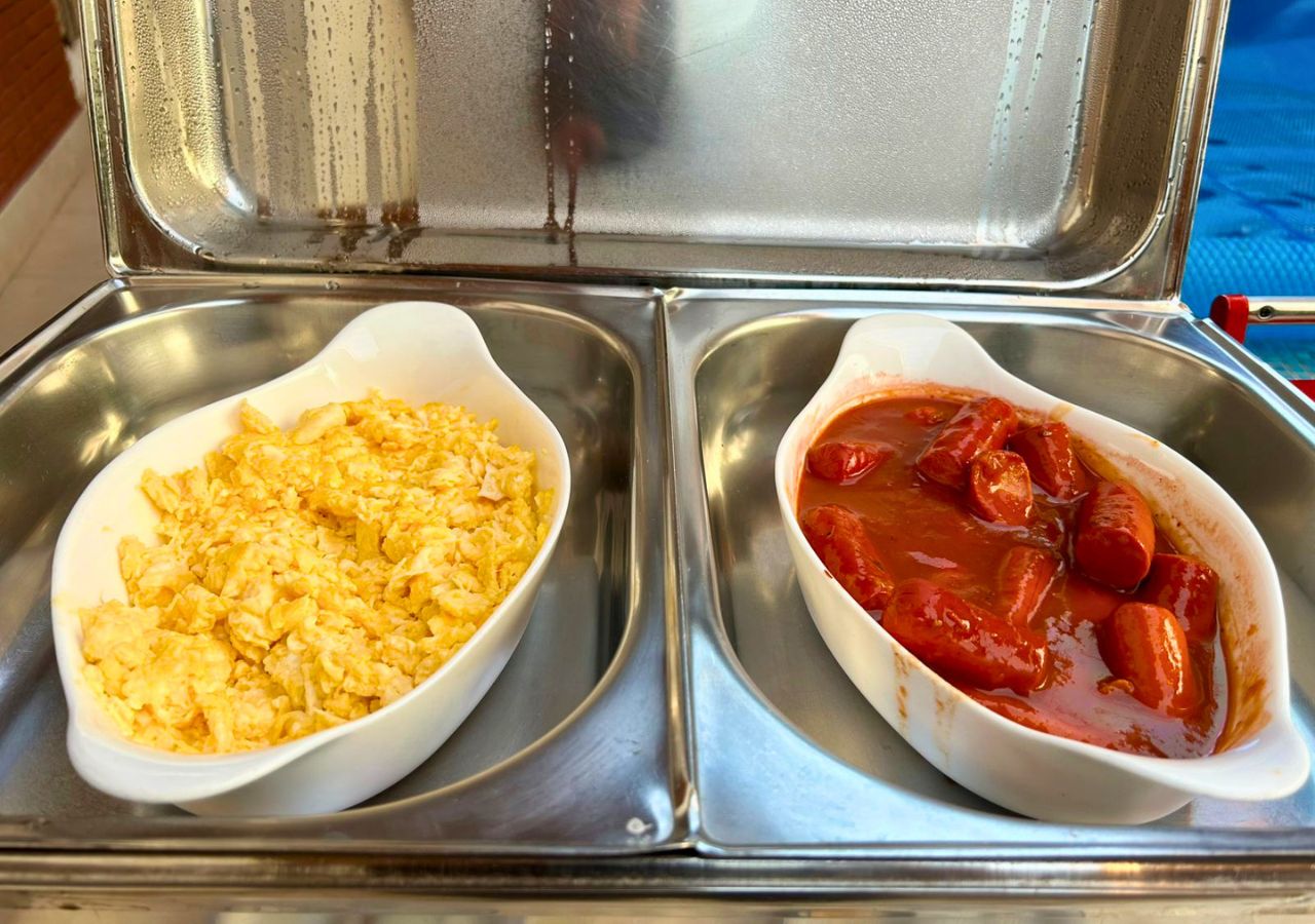Two white dishes on a metallic tray, one containing scrambled eggs and the other a red sauce with sausages.