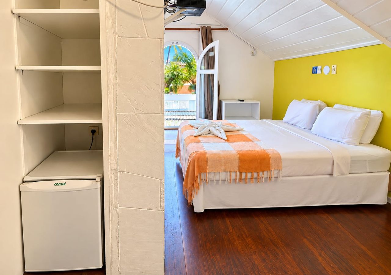 A bedroom with a bed, a bedside table, a small white cabinet, and a view of the outside.