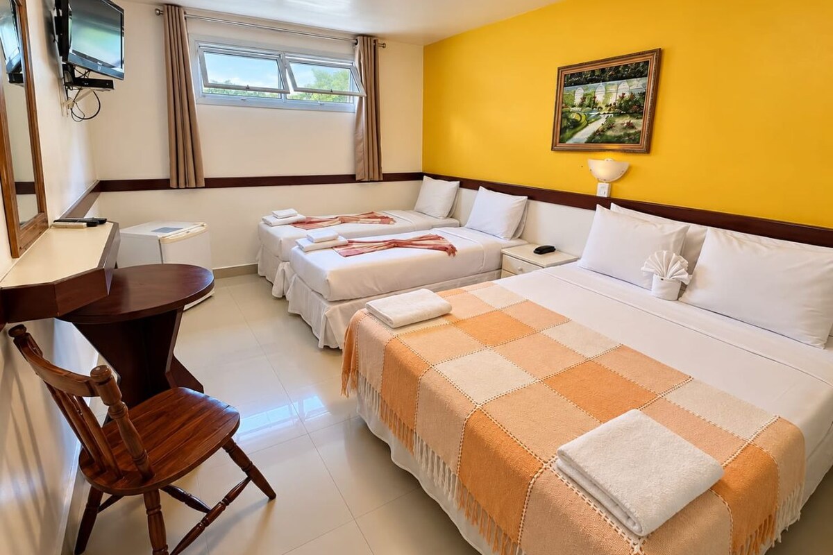 Une chambre d’hôtel avec deux lits, un bureau, une chaise, une télévision et une fenêtre avec des rideaux.