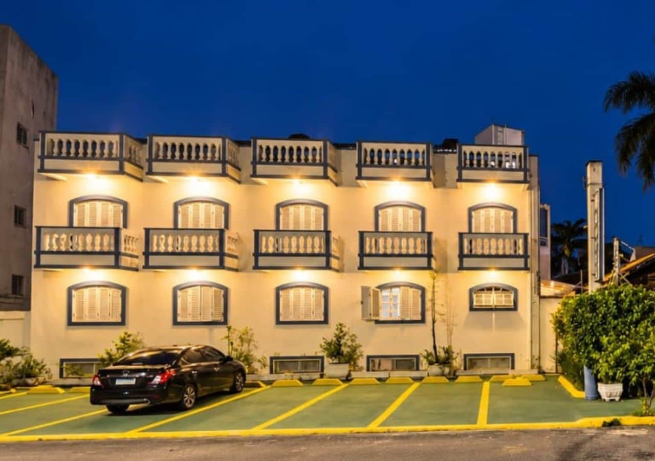 Un hotel de varios pisos con balcones, un área de estacionamiento y un coche estacionado al frente.