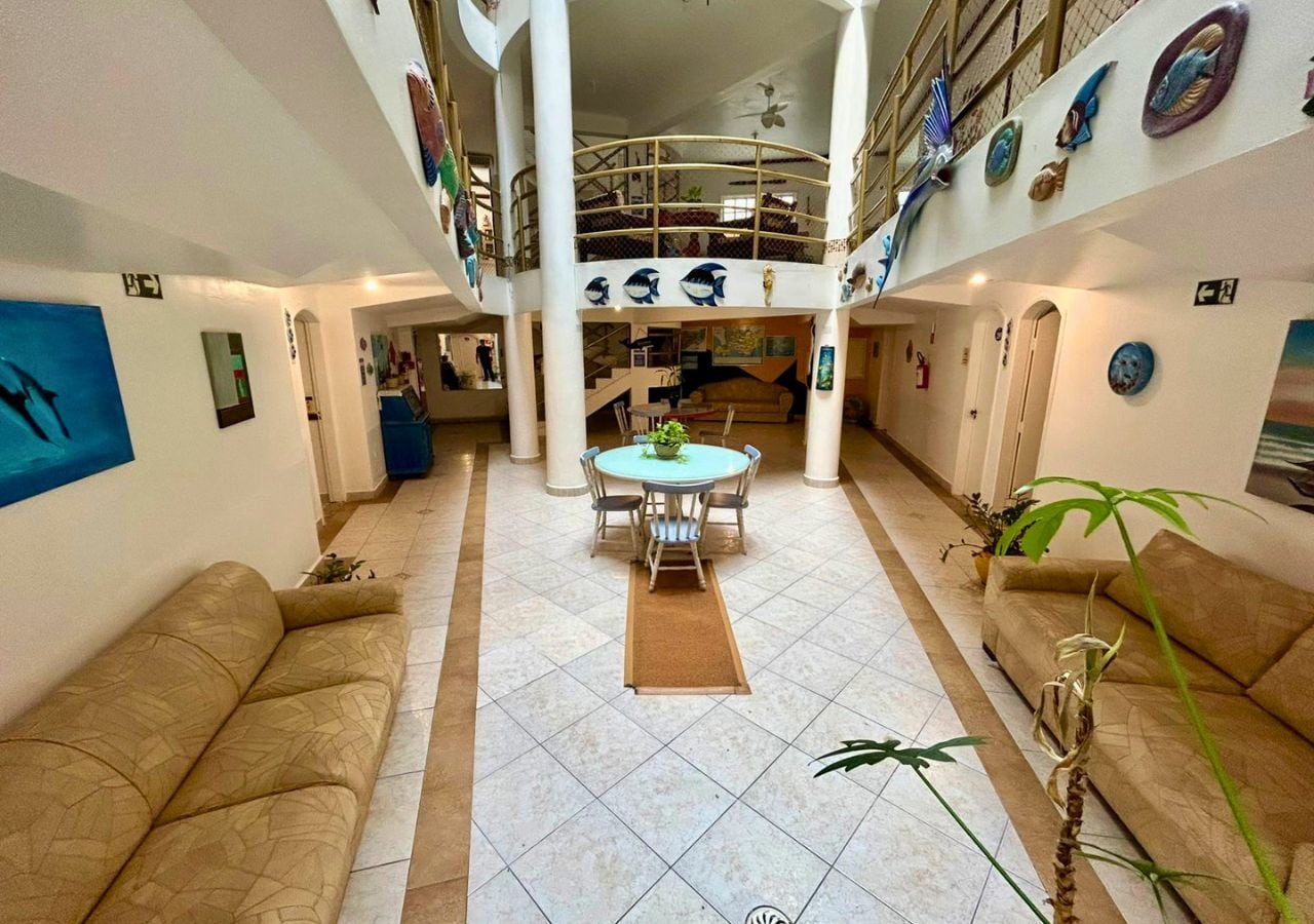 A spacious atrium with a central round table and chairs, surrounded by sofas and potted plants.
