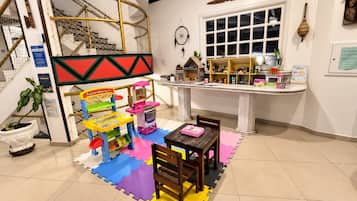 Espaço infantil com cozinha de brincar, loja de brinquedos e área de estar com mesa e cadeiras.