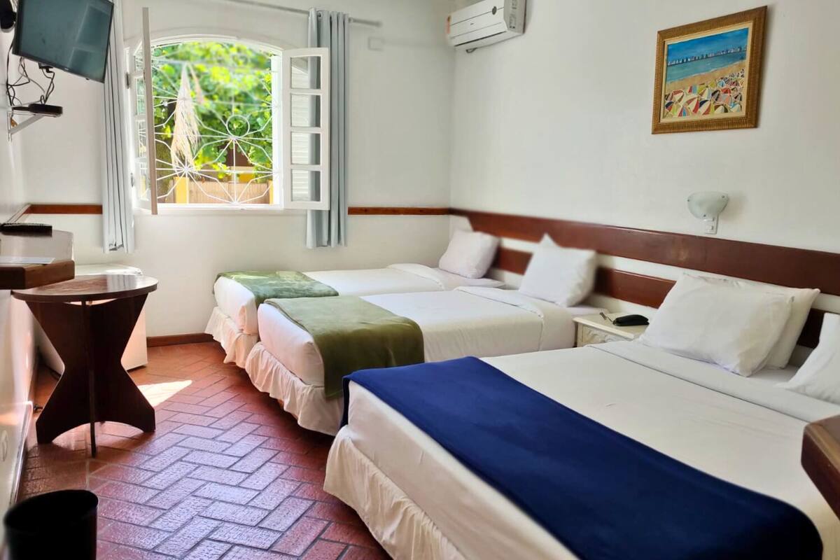 Une chambre d’hôtel avec deux lits, une télévision, une fenêtre avec des rideaux et un tableau au mur.