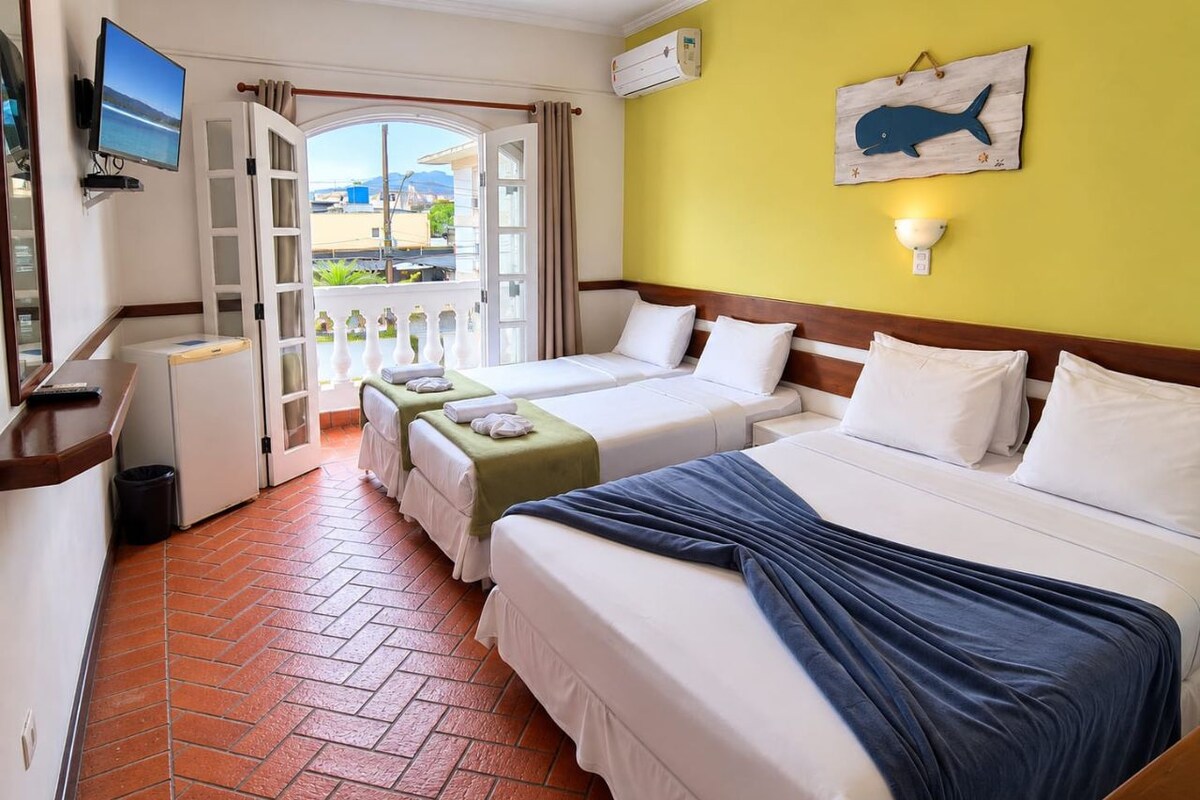 Une chambre d’hôtel avec deux lits, une télévision, un climatiseur fixé au mur et une vue sur l’extérieur, accessible par une porte ouverte.