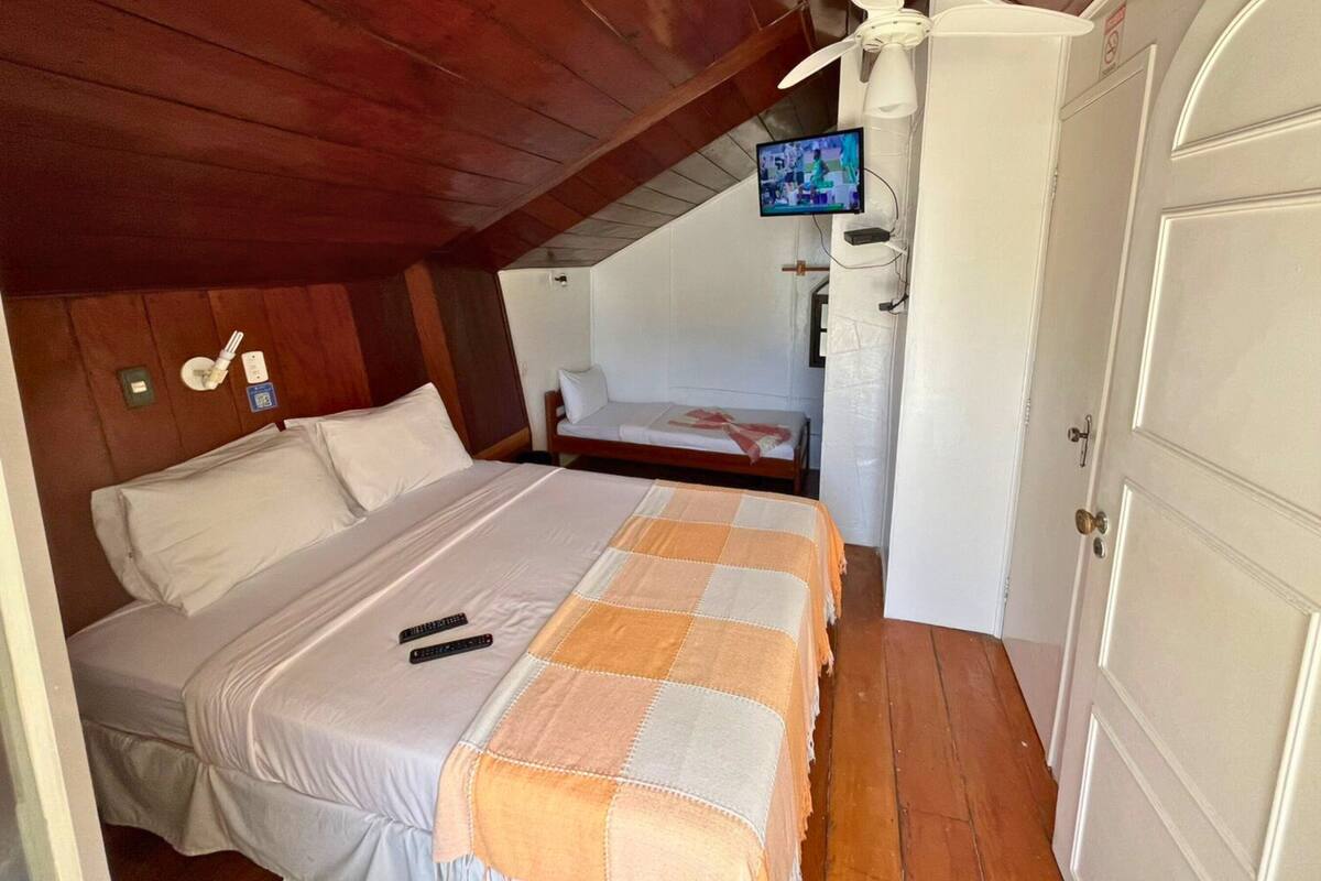 Une chambre à coucher avec un lit, un téléviseur fixé au mur, une porte et un ventilateur de plafond.