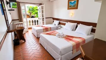 A hotel room with two beds, a TV, a small table, and a balcony with a view of greenery.