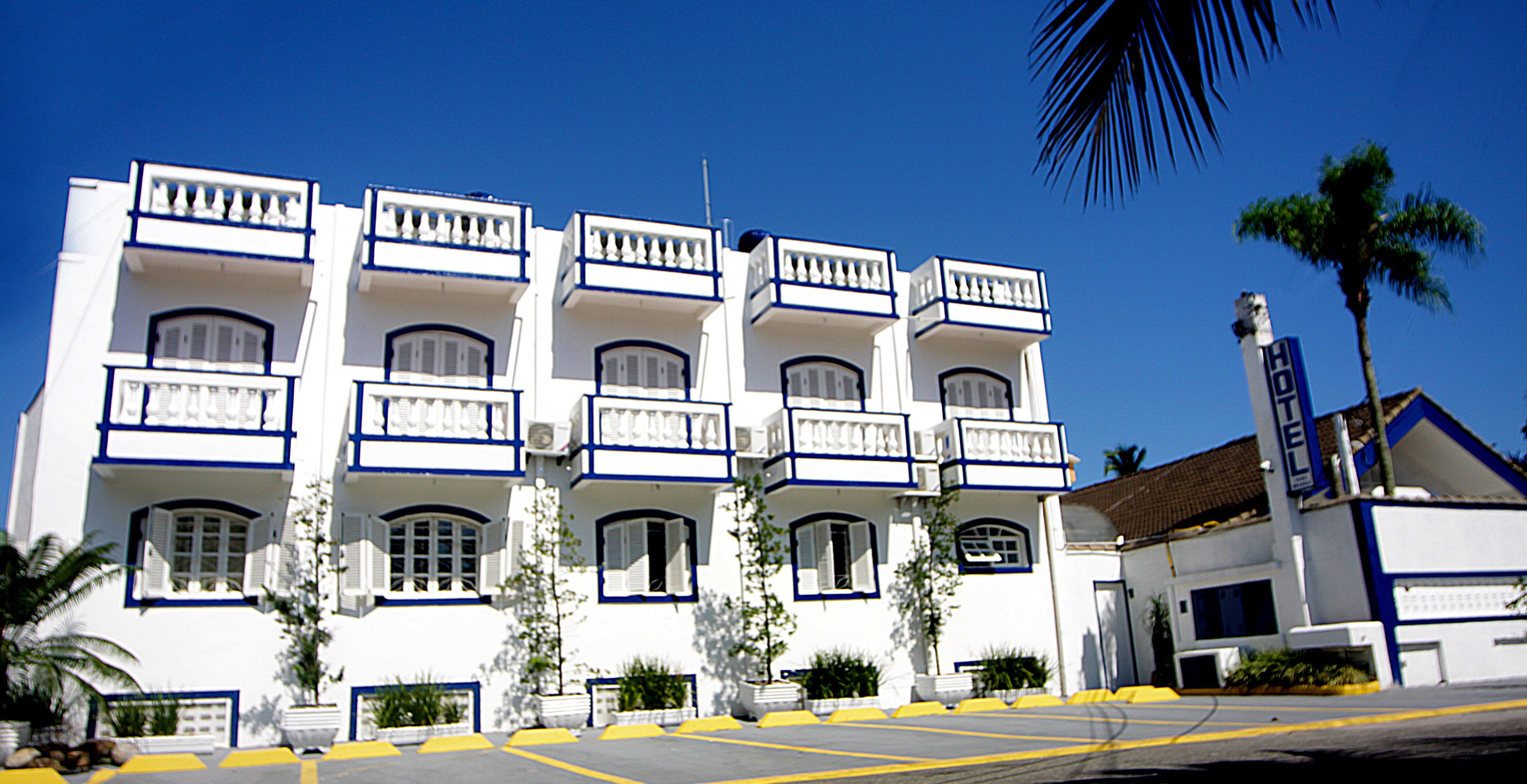 A white building with blue trim, multiple balconies, and a sign indicating it is a hotel.